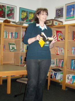 Lesungsfoto: Corinna Wieja steht mit dem Buch „Kommissar Unsichtbar“ in der Hand vor einem Bücherregal