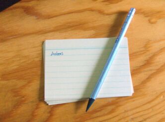 Karteikartenstapel auf dem ein Bleistift liegt. Auf der obersten Karteikarte steht das Wort „indoors“