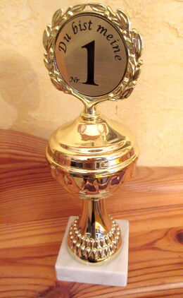 Goldener Pokal auf weißem Marmorsockel. Auf dem Pokal steht in einem goldenen Lorbeerkranz: „Du bist meine Nummer 1“